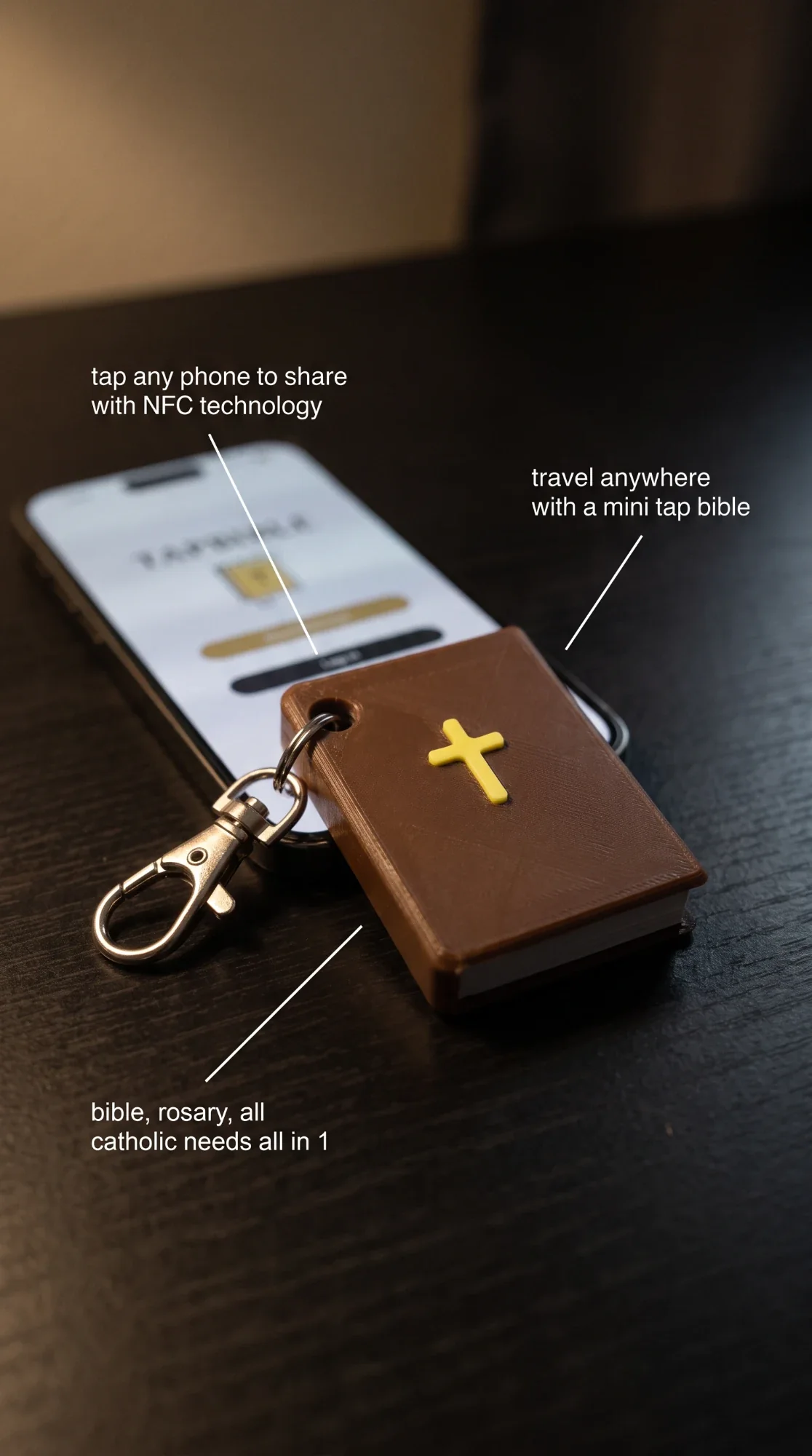 Brown TapBible keychain resting on a phone: tap any phone to share, travel anywhere, Bible and Rosary all in one