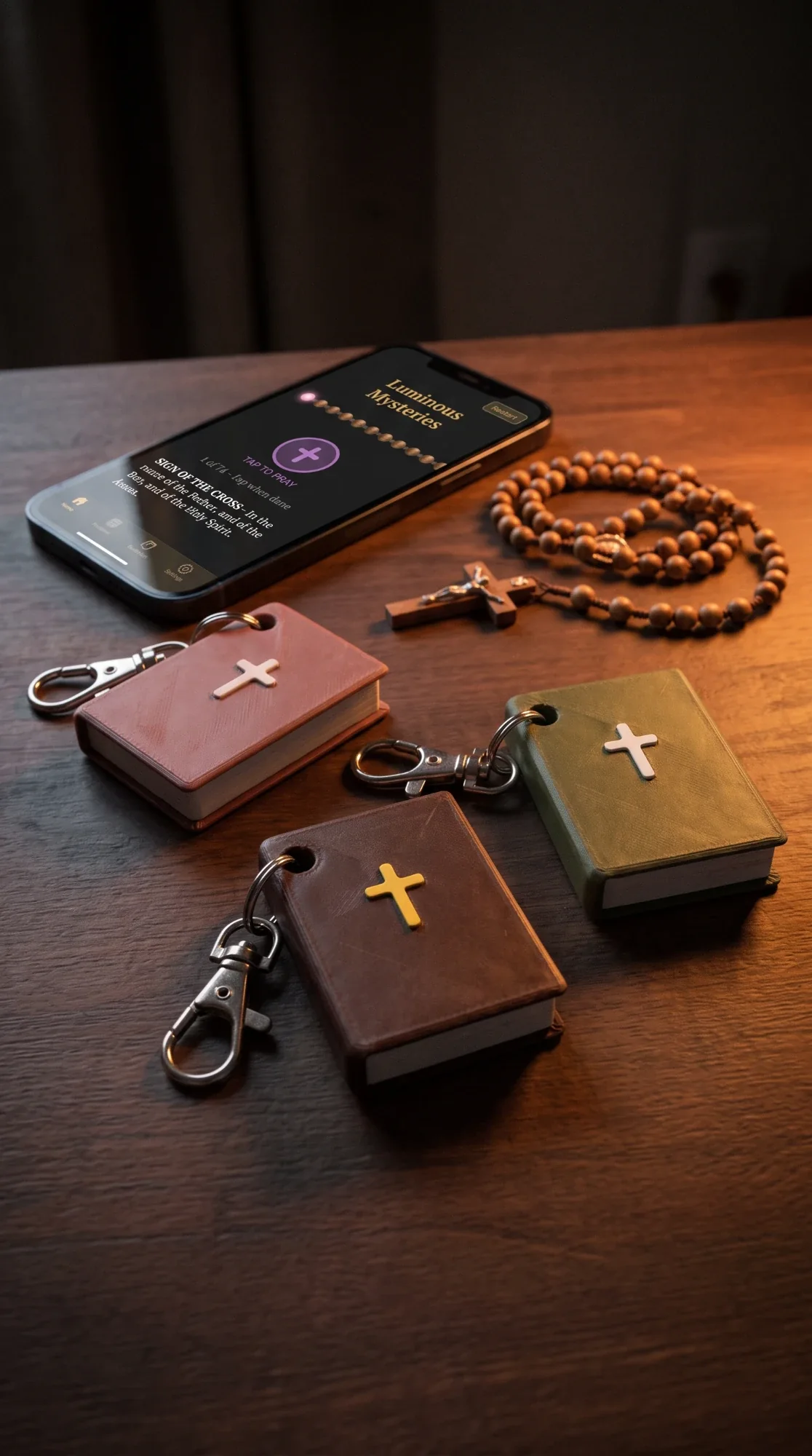 Rose, Brown and Sage TapBible keychains beside a wooden rosary and a phone showing the guided Rosary